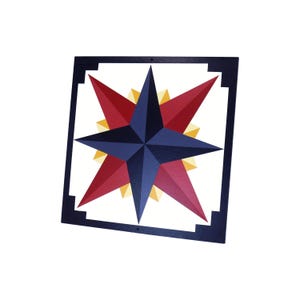 May include: A square, wooden wall art piece featuring a compass rose design. The compass rose has a navy blue center, red and yellow points, and is framed by a dark blue square border. The artwork is designed to be hung on a wall.