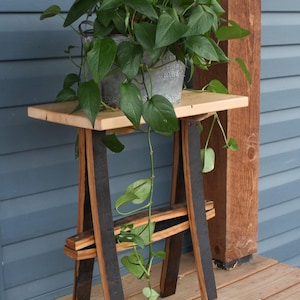 May include: A wooden table made from repurposed wine barrels with a light wood top. A potted plant with green leaves hangs over the side of the table.