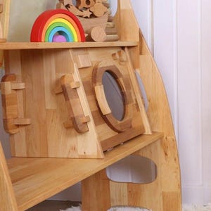 May include: A wooden playhouse with a built-in washing machine, a shelf, and a rainbow toy on top. The playhouse is made of natural wood and has a simple, modern design.