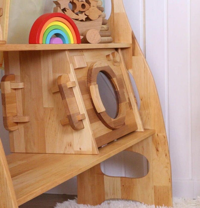 May include: A wooden playhouse with a built-in washing machine, a shelf, and a rainbow toy on top. The playhouse is made of natural wood and has a simple, modern design.