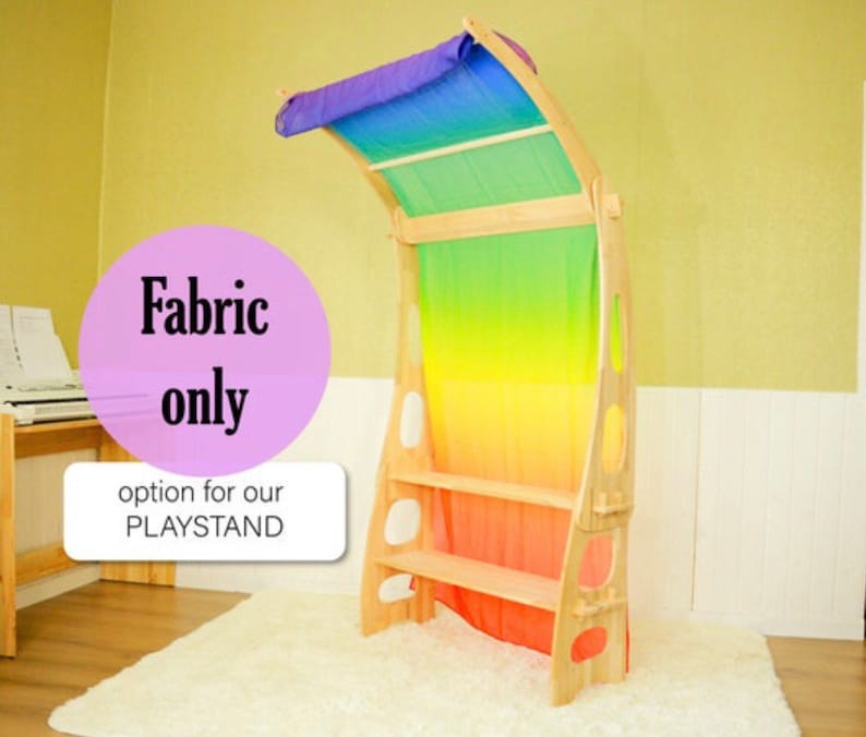 May include: Rainbow fabric play curtain with a wooden frame and shelves. The fabric is a gradient of colors from purple to red. The text "Fabric only" and "option for our PLAYSTAND" is printed on a pink circle.