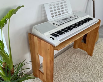 Könnte beinhalten: Weiße elektronische Tastatur mit Notenständer auf einem Holzständer. Die Tastatur steht auf einem weißen, flauschigen Teppich.