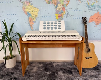 Könnte beinhalten: Eine weiße Tastatur mit einem Holzständer und einer braunen Akustikgitarre. Die Tastatur steht auf dem Ständer und die Gitarre lehnt an dem Ständer. Der Ständer steht vor einer Weltkarte.