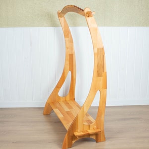 K&ouml;nnte beinhalten: Ein Harfenst&auml;nder aus Holz mit einer gebogenen Oberseite und einem Regal zum Aufbewahren von Musik. Der St&auml;nder ist aus hellem Holz gefertigt und hat eine nat&uuml;rliche Oberfl&auml;che.