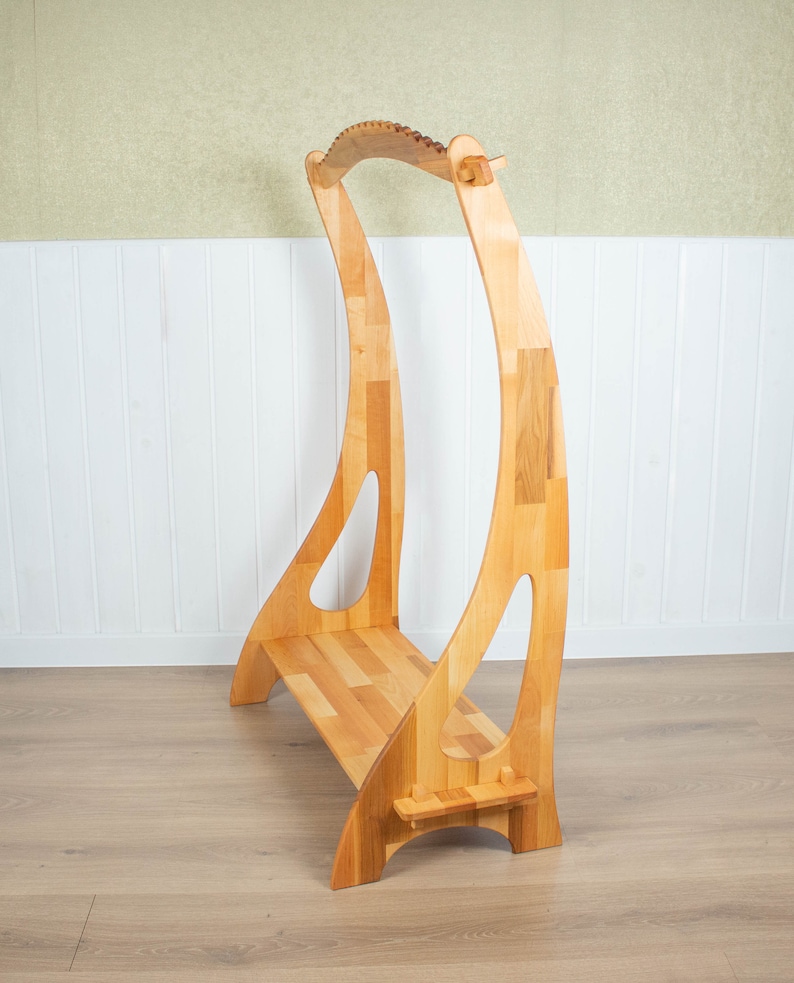 K&ouml;nnte beinhalten: Ein Harfenst&auml;nder aus Holz mit einer gebogenen Oberseite und einem Regal zum Aufbewahren von Musik. Der St&auml;nder ist aus hellem Holz gefertigt und hat eine nat&uuml;rliche Oberfl&auml;che.