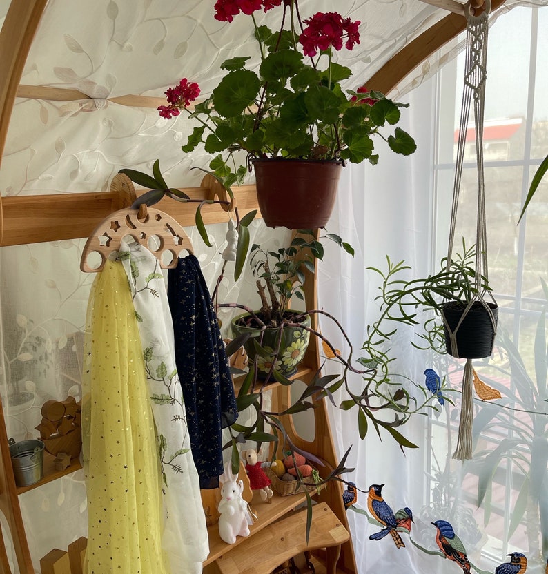 May include: A wooden rack with two scarves hanging on it. The rack is decorated with a crescent moon and stars. There are plants and flowers in pots hanging from the rack.