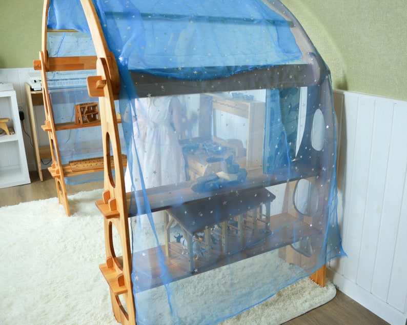 May include: A wooden play structure with shelves and a blue sheer curtain with gold stars. The structure is designed for children's play and is made of natural wood.