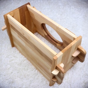 May include: A wooden box with a cutout in the front and a latch on the side. The box is made of light wood and has a natural finish.