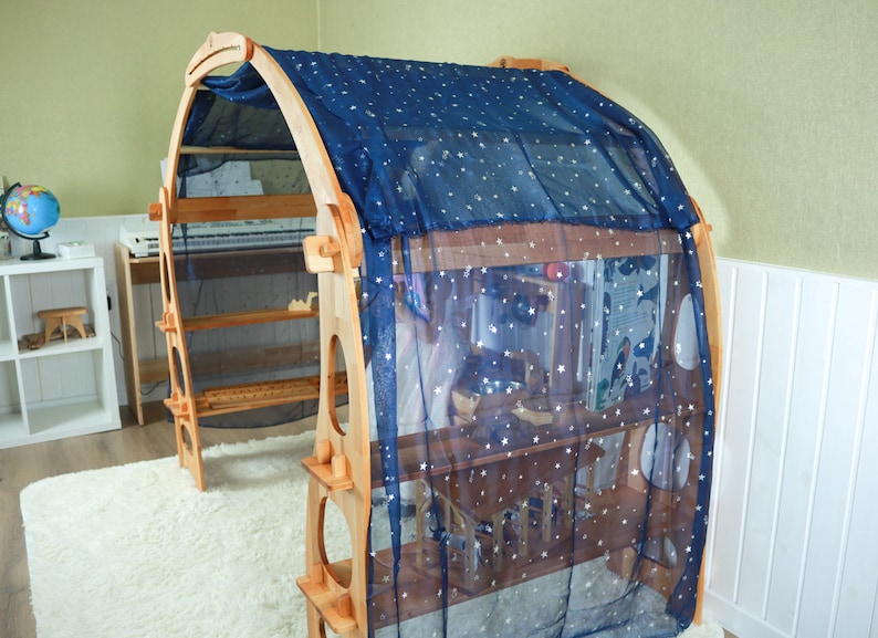 May include: A wooden play structure with shelves and a blue fabric canopy with white stars. The canopy is draped over the top of the structure, creating a cozy and inviting space for play.