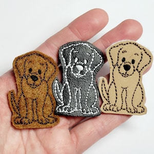 May include: Three felt dog appliques in brown, black, and tan. The dogs are sitting with their paws together and their tails curled behind them. The dogs have embroidered details, including eyes, noses, and mouths.