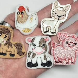 May include: A collection of six embroidered farm animal patches. The patches include a brown and tan pony, a white and brown cow, a pink pig, a white chicken, and a white lamb. Each patch is made of felt and has embroidered details.