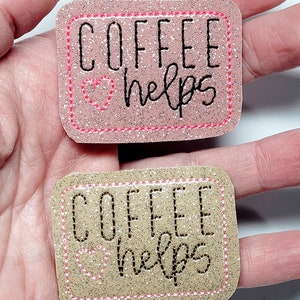 May include: Two iron-on patches with pink and gold glitter. Both patches have a pink heart and the text "Coffee helps" in black.