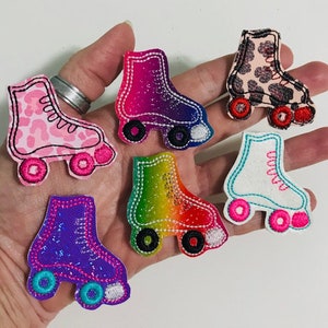 May include: Six embroidered iron-on patches of roller skates in various colors and patterns, including pink with leopard print, rainbow, purple, white with blue trim, and pink with white trim.