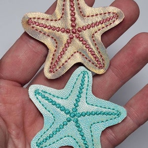 May include: Two embroidered starfish patches. One is gold with pink stitching and the other is light blue with teal stitching.