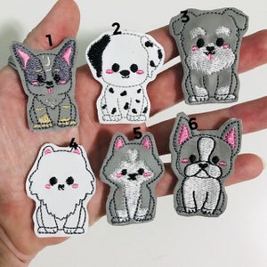 May include: Set of ten iron-on patches featuring different dog breeds. The patches are gray with white and black embroidery. The dogs are all sitting and have cute expressions.