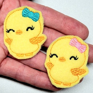 May include: Two yellow felt chick appliques with embroidered details. One chick has a teal bow and the other has a pink bow.
