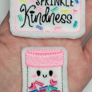 May include: Two embroidered patches, one with the text "Sprinkle Kindness" surrounded by colorful sprinkles, and the other with a cartoon jar filled with colorful sprinkles.