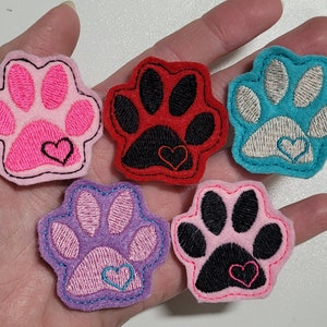 May include: Five felt paw print patches with a heart in the center. The paw prints are pink, purple, red, black, and turquoise.