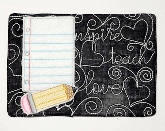 May include: Black fabric notepad with a white lined paper insert and a yellow pencil with a pink eraser. The fabric has white stitching that says "inspire teach love" with hearts and swirls.
