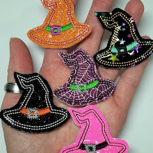 May include: Five witch hats in different colors and patterns. The hats are made of felt and have a glitter finish. The hats are all different sizes and shapes.
