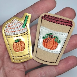 May include: Two embroidered patches featuring fall-themed drinks. The first patch is a gold-colored coffee cup with a pumpkin design. The second patch is a brown coffee cup with a white pumpkin design.