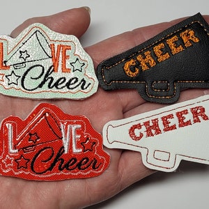 May include: Three embroidered iron-on patches featuring a megaphone with the text "Love Cheer". One patch is white with orange text, one is red with white text, and one is black with orange text.