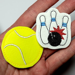 May include: Two felt patches, one with a yellow tennis ball and the other with a white bowling pin design. The bowling pin design has three pins and a black bowling ball with red and blue accents.