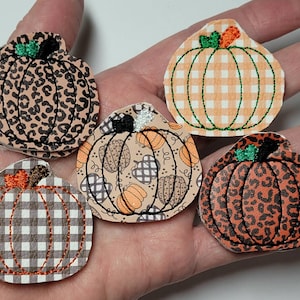 May include: Five felt pumpkin patches with different patterns. One pumpkin is orange and white gingham, one is brown and black leopard print, one is orange and black leopard print, one is brown and white gingham, and one is orange with a brown and white pattern.