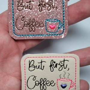 May include: Two embroidered patches with the text "But first, Coffee" and a stylized coffee cup. The top patch is pink with turquoise stitching and a pink heart on the coffee cup. The bottom patch is beige with pink stitching and a purple heart on the coffee cup.