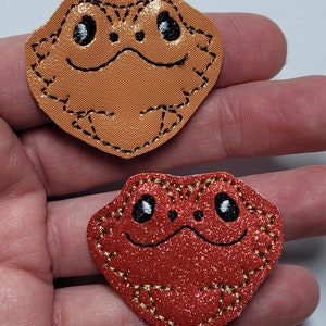 May include: Two embroidered bearded dragon patches. One is orange and the other is red with glitter.