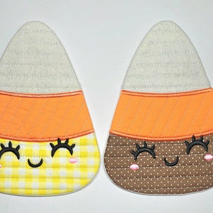 May include: Two felt candy corn ornaments with embroidered faces. One is yellow and white with orange stripes, the other is brown with orange stripes.