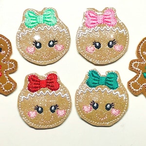 May include: Five felt gingerbread people ornaments. Two are round with a white icing border and a bow on top. One has a red bow, one has a green bow, one has a pink bow, and one has a teal bow. The other two are gingerbread people with a red and green bow.