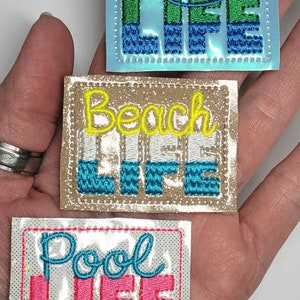 May include: Three embroidered iron-on patches with the words "Lake Life", "Beach Life", and "Pool Life". The patches are on a white background with a glittery finish.
