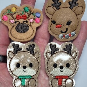 May include: Four felt Christmas reindeer ornaments. Two are brown with black antlers and a red nose. Two are beige with black antlers and a green or red scarf.