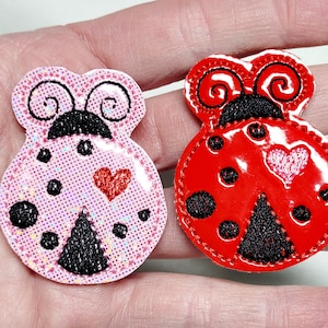 May include: Two ladybug-shaped patches. One is pink with black spots and a red heart, the other is red with black spots and a heart. Both have black antennae and are embellished with black stitching.