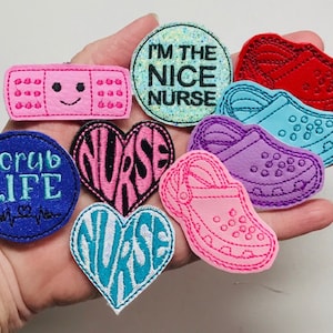 May include: A set of 10 embroidered iron-on patches featuring a variety of designs related to the nursing profession. The patches include a heart with the word "Nurse", a band-aid with a smiley face, a pair of clogs, and a circle with the text "I'm the Nice Nurse".