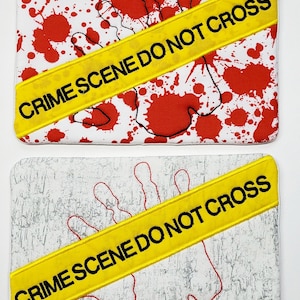 May include: Two white fabric coasters with a red handprint and yellow "CRIME SCENE DO NOT CROSS" tape. The top coaster has red splatter paint and the bottom coaster has a gray textured background.
