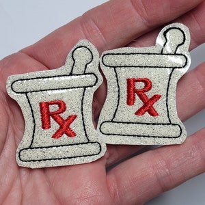 May include: Two white, glitter-covered, felt patches with an embroidered mortar and pestle design. The mortar and pestle are outlined in black and have a red "Rx" in the center.
