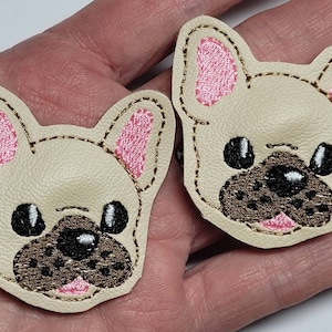 May include: Two beige felt French bulldog appliques with pink ears and black eyes. The appliques are embroidered with gold thread.