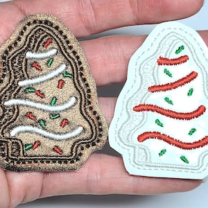 May include: Two embroidered Christmas tree patches. One is brown with white frosting and red and green sprinkles. The other is white with red frosting and green sprinkles.