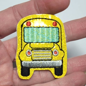 May include: A yellow school bus patch with red lights, a blue window, and a silver grill. The patch is made of glitter fabric.