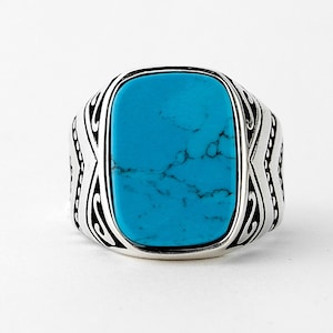 May include: A silver ring with a turquoise stone set in a decorative frame.