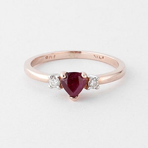 Könnte beinhalten: Ein Ring aus Roségold mit einem herzförmigen Rubin und zwei kleineren Diamanten auf jeder Seite.