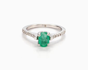 May include: A silver ring with a green oval emerald gemstone and a row of small diamonds around the band.
