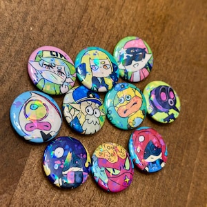 K&ouml;nnte beinhalten: Eine Sammlung von zehn bunten, runden Kn&ouml;pfen mit Cartoon-Charakter-Designs. Die Kn&ouml;pfe zeigen eine Vielzahl von Charakteren in leuchtenden Farben, darunter Rosa, Blau, Gelb und Gr&uuml;n, mit holografischen Akzenten. Die Kn&ouml;pfe sind auf einer Holzoberfl&auml;che angeordnet.