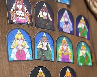 May include: A set of 11 illustrated stickers featuring different characters from the Legend of Zelda video game series. The stickers are in a stained glass style with a triangular design and feature characters like Link, Zelda, and Ganondorf.