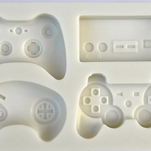 May include: A white silicone mold for making chocolate or candy in the shape of four different video game controllers. The mold includes a classic NES controller, a Playstation controller, an Xbox controller, and a Sega Genesis controller.