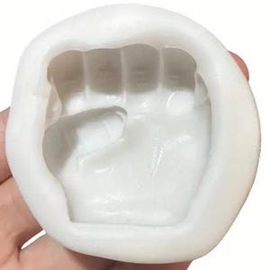 May include: White silicone mold shaped like a closed fist. The mold is designed for making edible replicas of a hand.