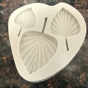 May include: A white silicone mold with three leaf shapes. The leaves have a ribbed texture.