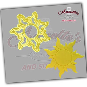 May include: Two yellow sun-shaped cookie cutters. One is a solid sun shape and the other is a detailed sun with a cutout center.